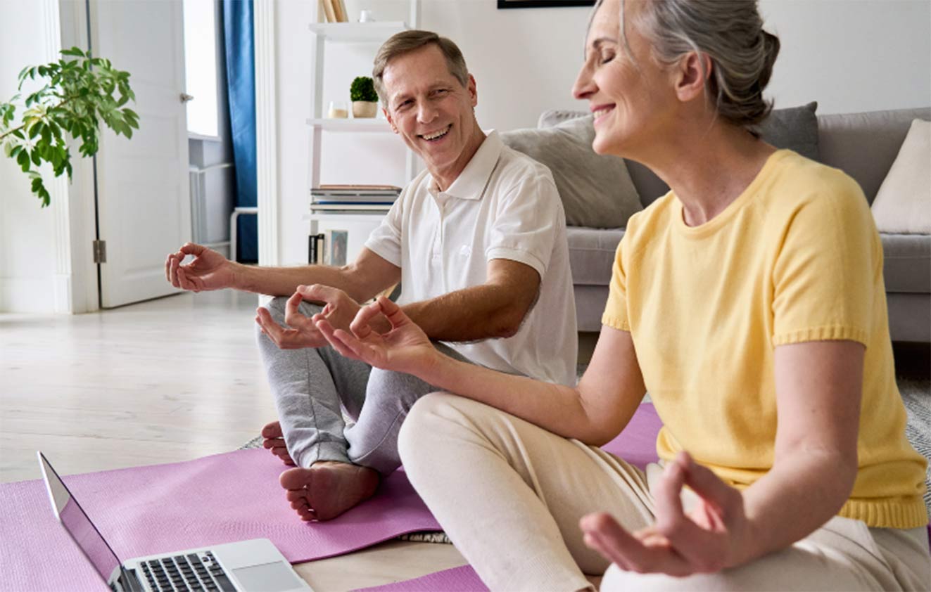 En man och en kvinna som sitter i skräddarställning framför en dator och utövar yoga